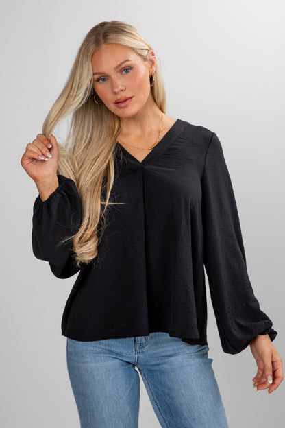 Woman wearing a black blouse and blue jeans against a gray background