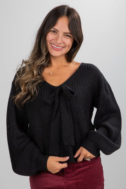 Woman wearing a black sweater with a bow tie on a gray background