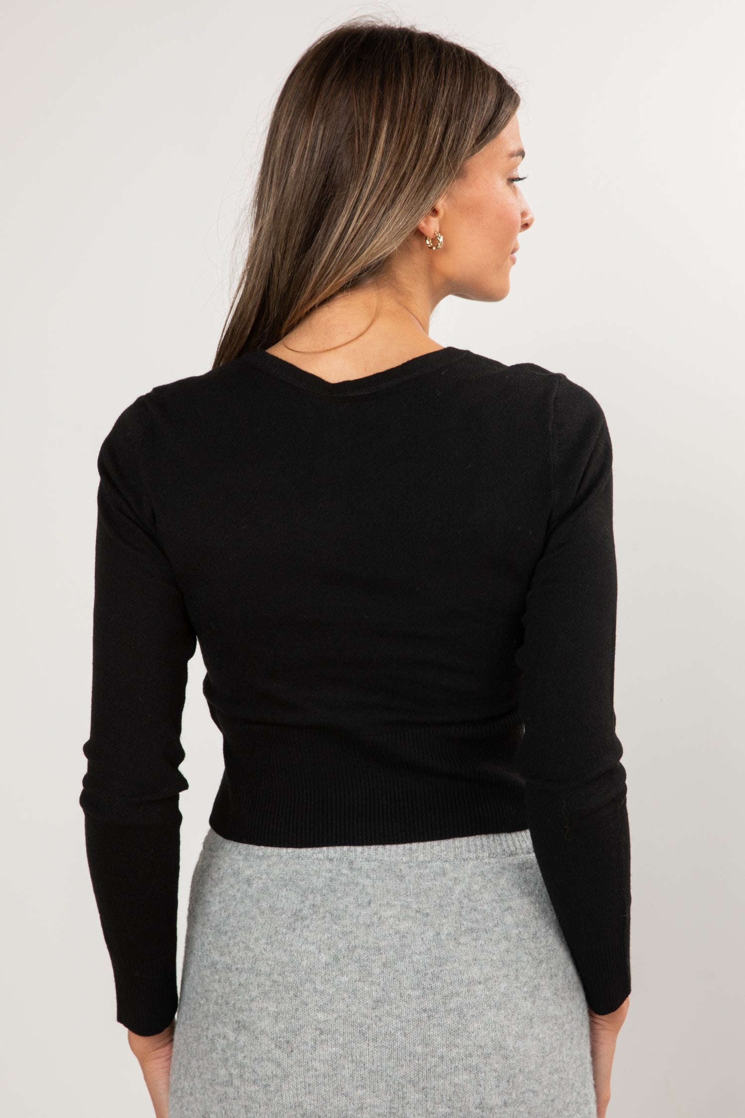 Woman wearing a black long-sleeve top and gray skirt on a white background