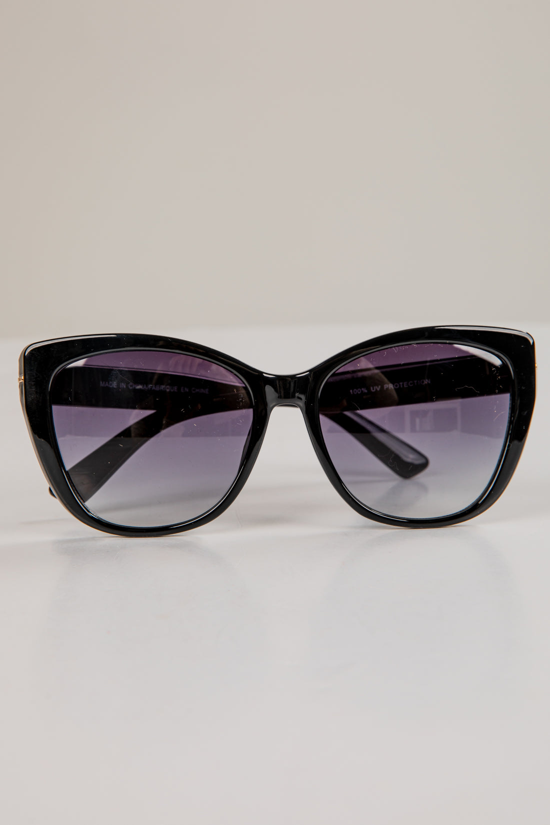 Black cat-eye sunglasses with purple-tinted lenses on a light gray background