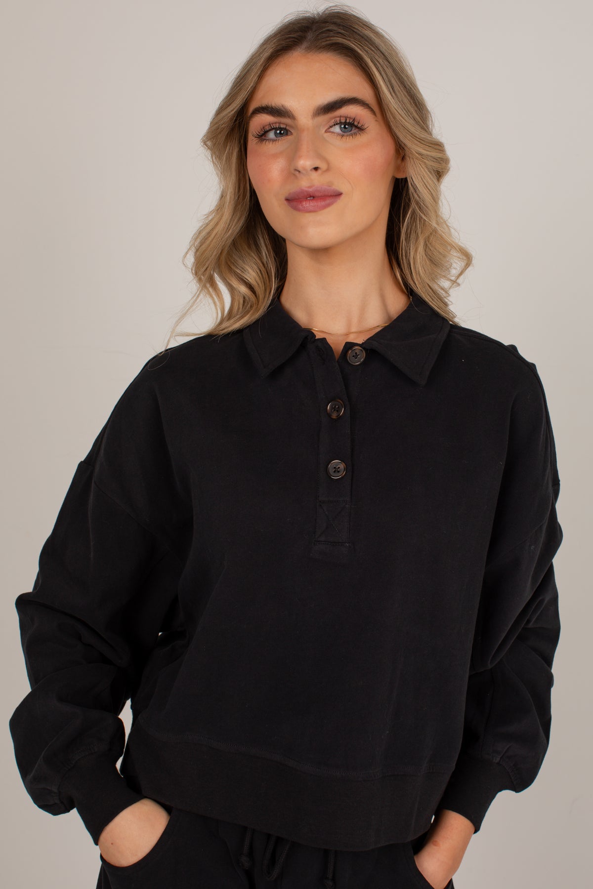 A woman wearing a black long-sleeve polo shirt with a three-button placket, photographed against a plain light gray studio background.