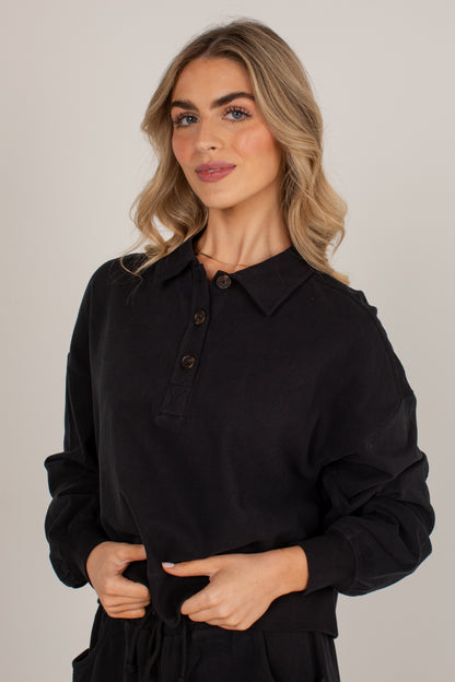 A woman modeling a black long-sleeve collared shirt with a button placket, photographed against a plain light gray studio background.