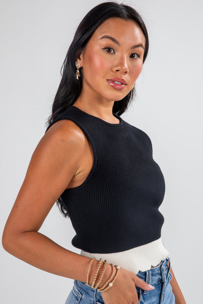 Woman wearing a black sleeveless top and light blue jeans against a plain background