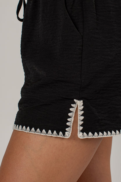 Close-up of black shorts with a white zigzag stitched trim along the hem, shown on a model&