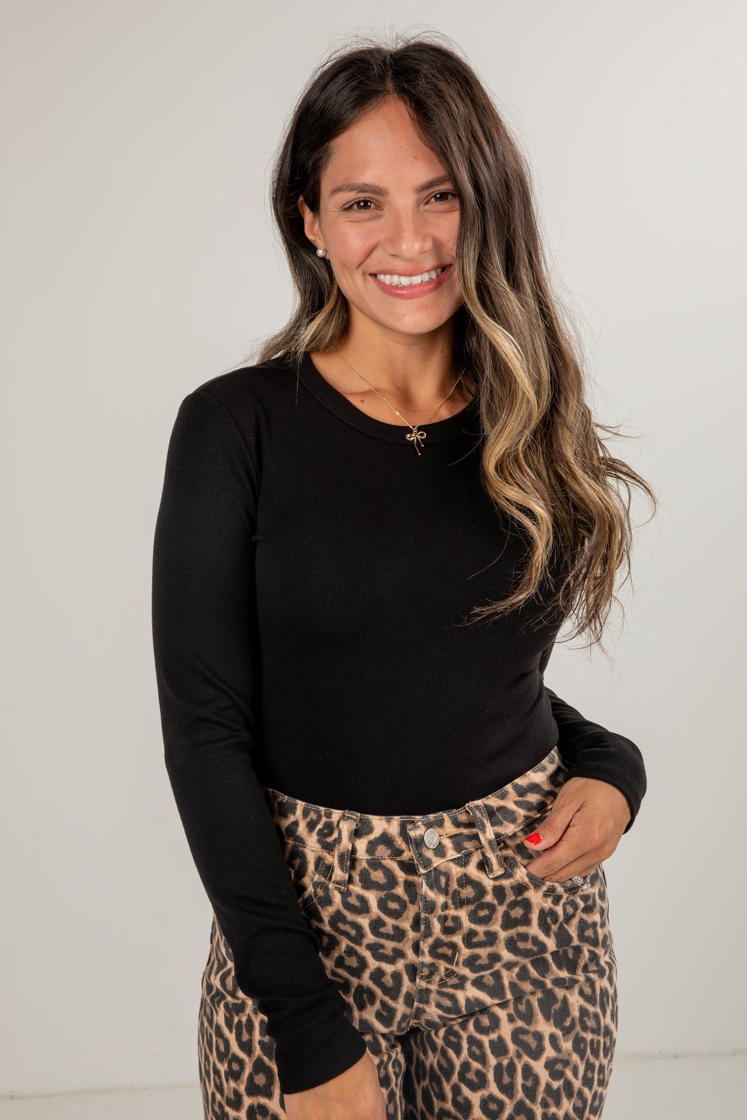 Woman wearing a black long-sleeve top and leopard print pants against a white background