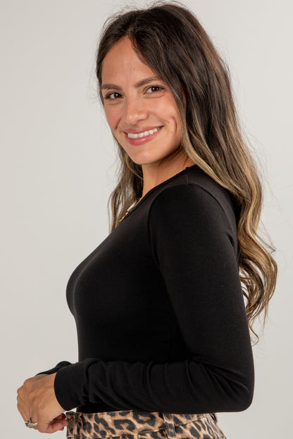Woman wearing a black long-sleeve top with a plain background