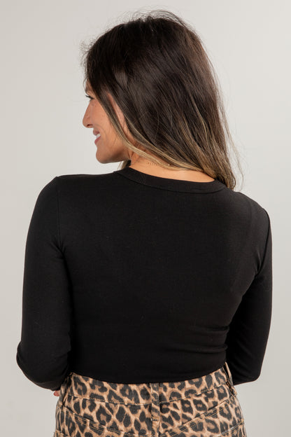 Woman wearing a black long-sleeve top and leopard print pants on a plain background