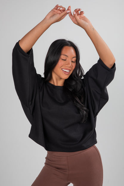 Woman wearing a black top and brown pants against a plain background