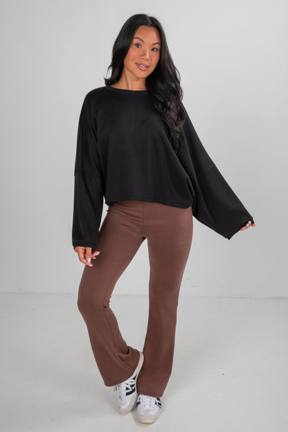 Woman wearing a black top and brown pants on a white background