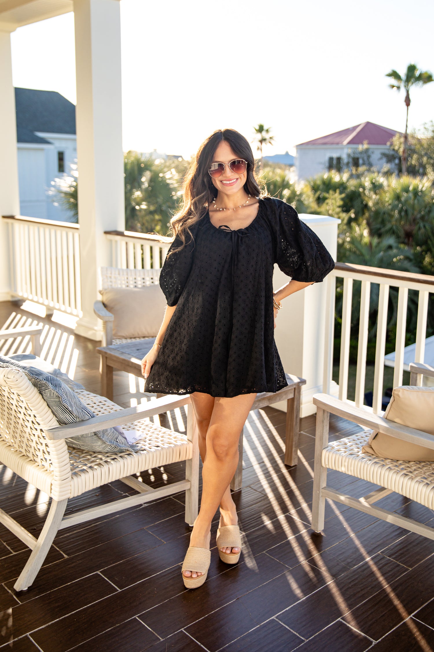 Woman in a black dress standing on a balcony with chairs and a scenic background