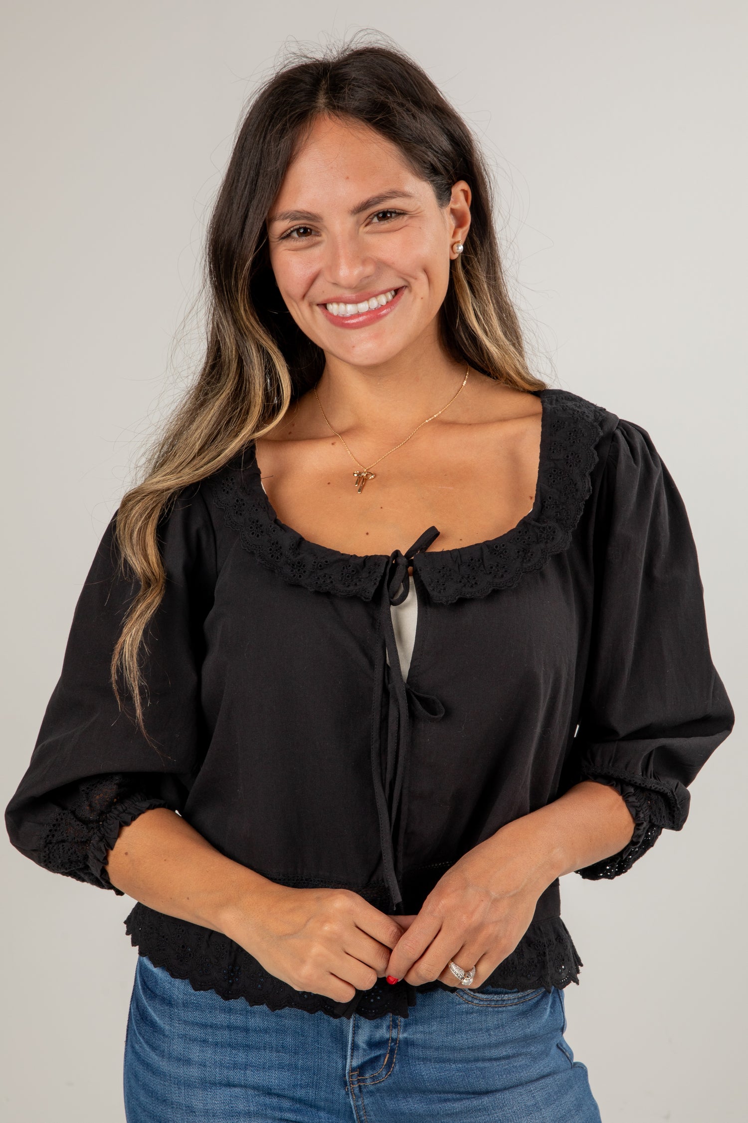 Woman wearing a black blouse with ruffled details on a plain background