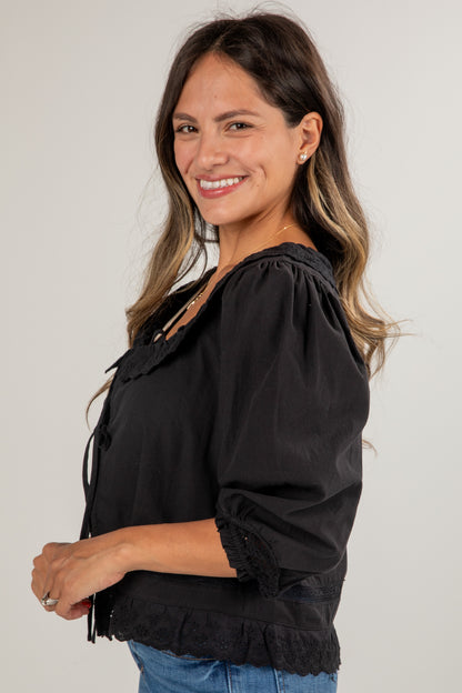 Woman wearing a black blouse with ruffled details on a plain background