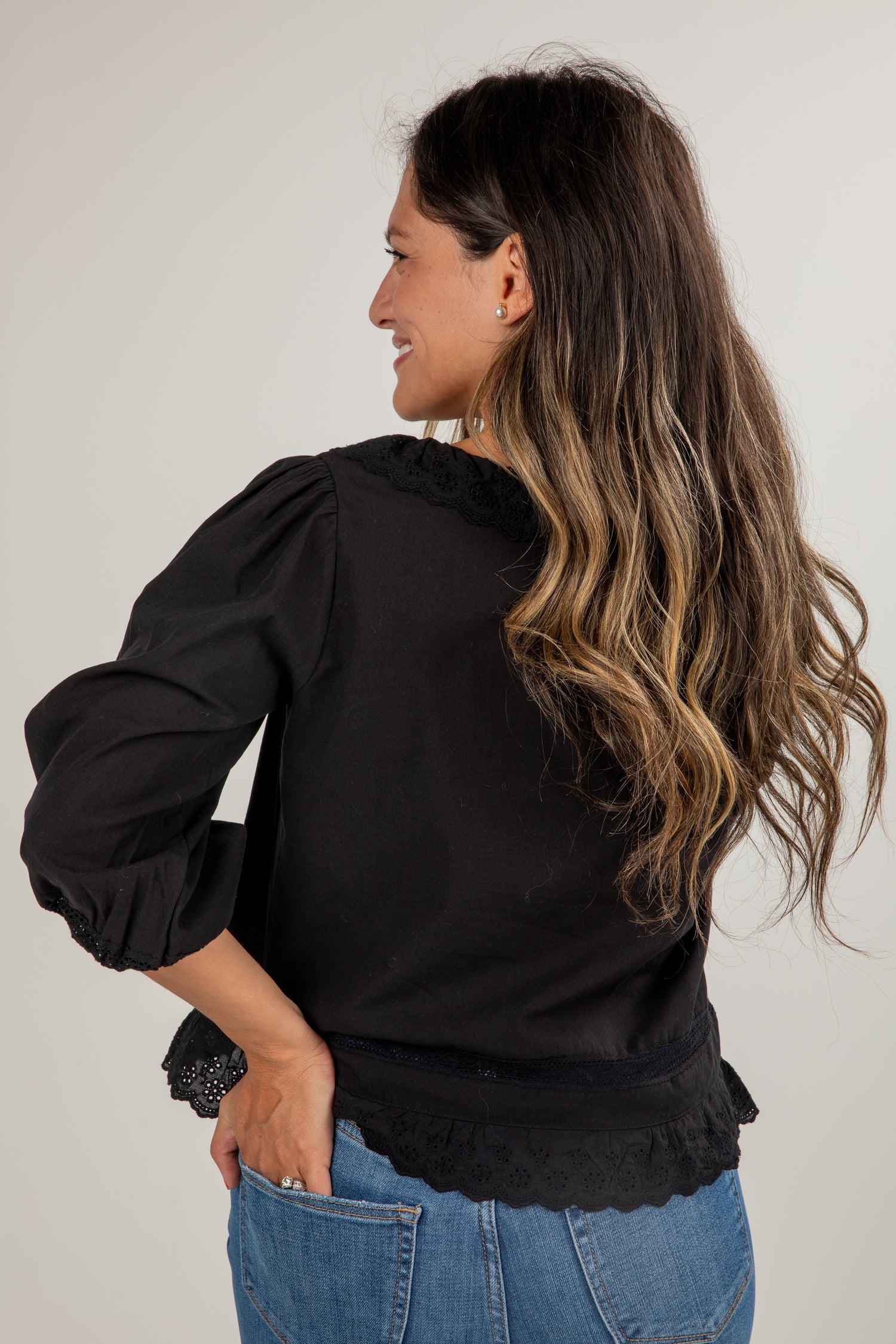 Woman wearing a black blouse with ruffled details and blue jeans on a plain background