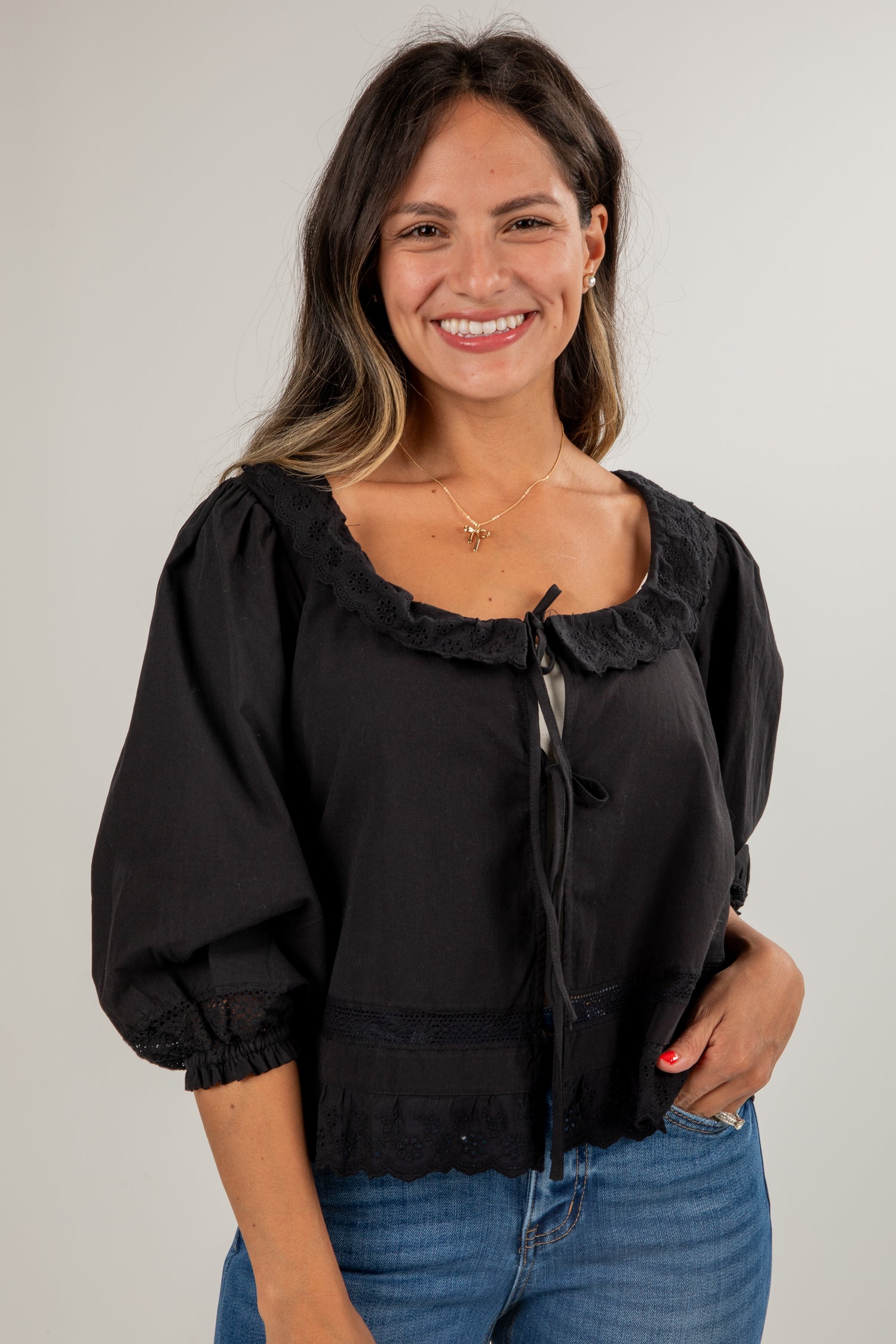 Woman wearing a black blouse with ruffled details and blue jeans on a plain background