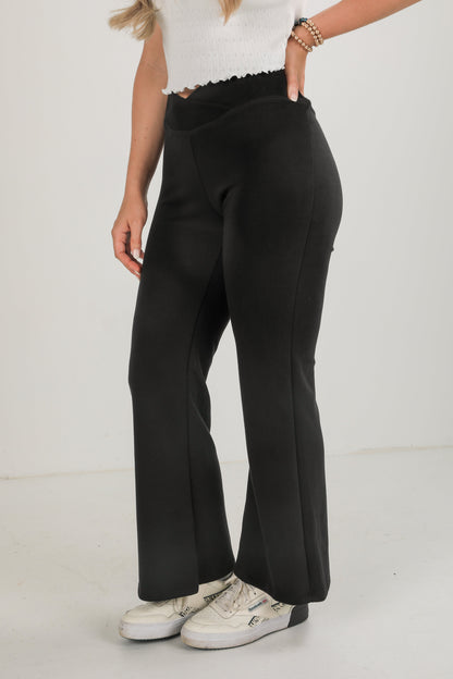 Person wearing black wide-leg pants and white sneakers on a light background