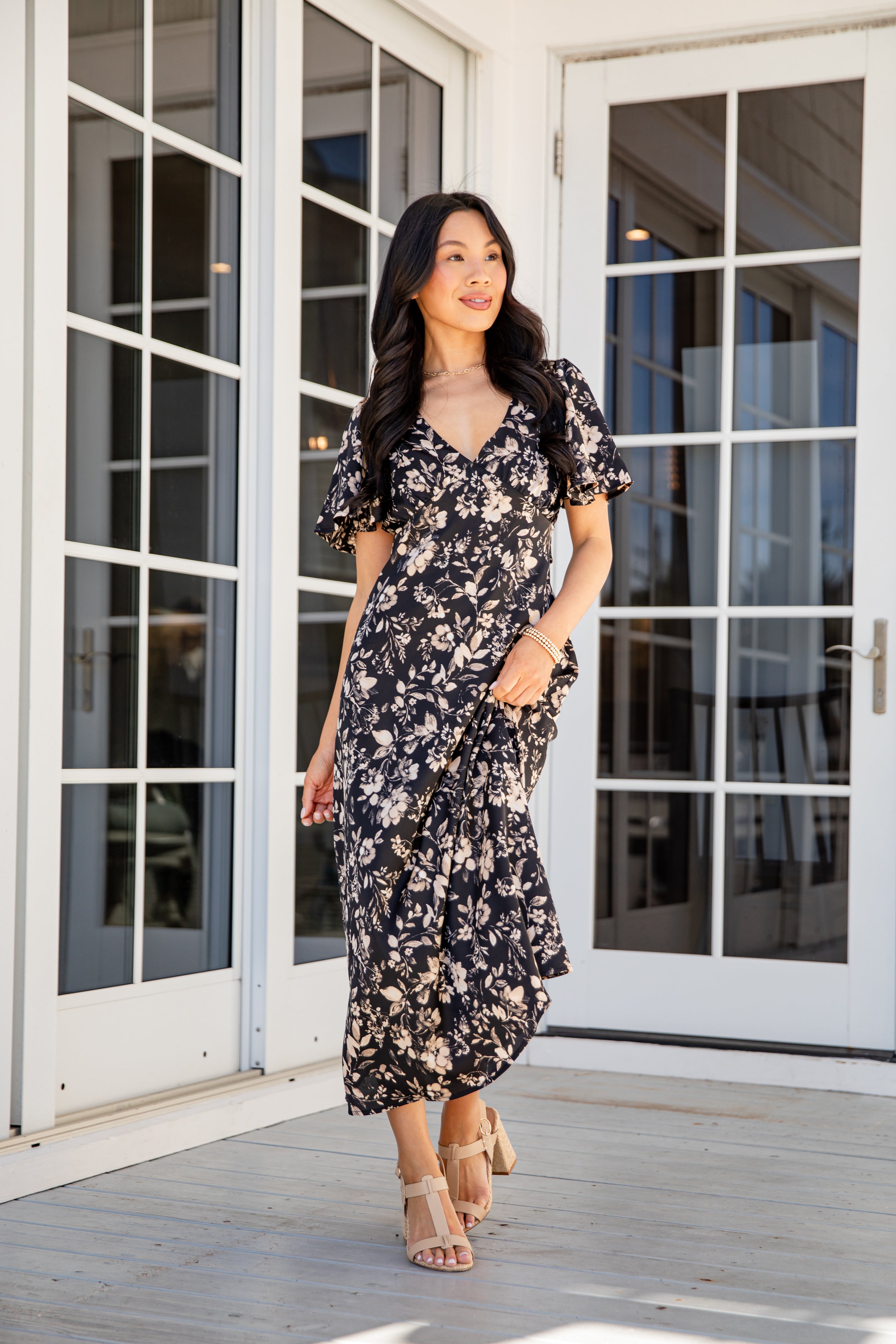 Woman in a floral dress standing on a wooden deck with glass doors in the background