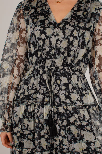 A close-up of a woman wearing a long-sleeve V-neck dress with a black, beige, and gray floral pattern and a matching waist tie.