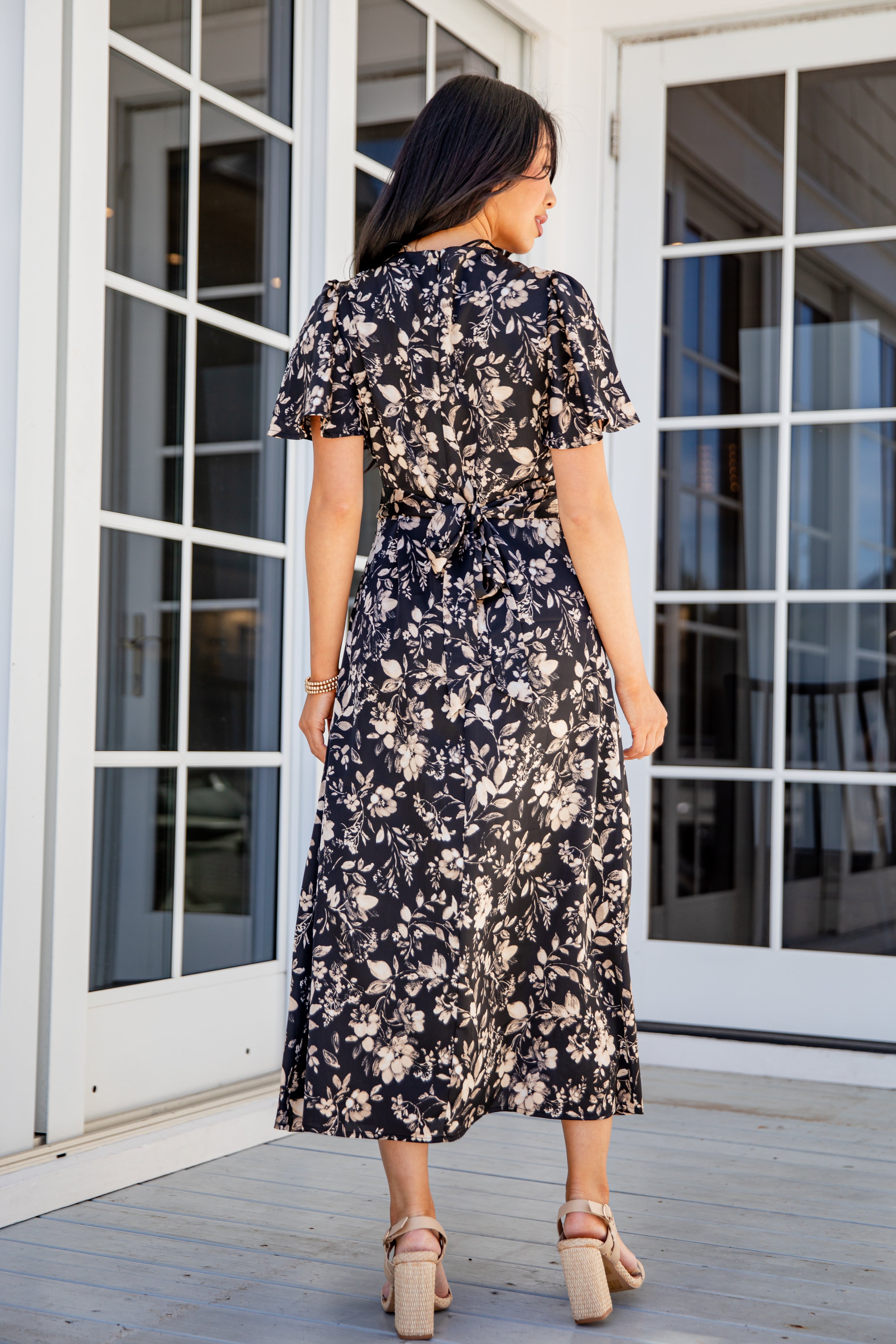 Woman wearing a floral dress standing on a wooden deck.