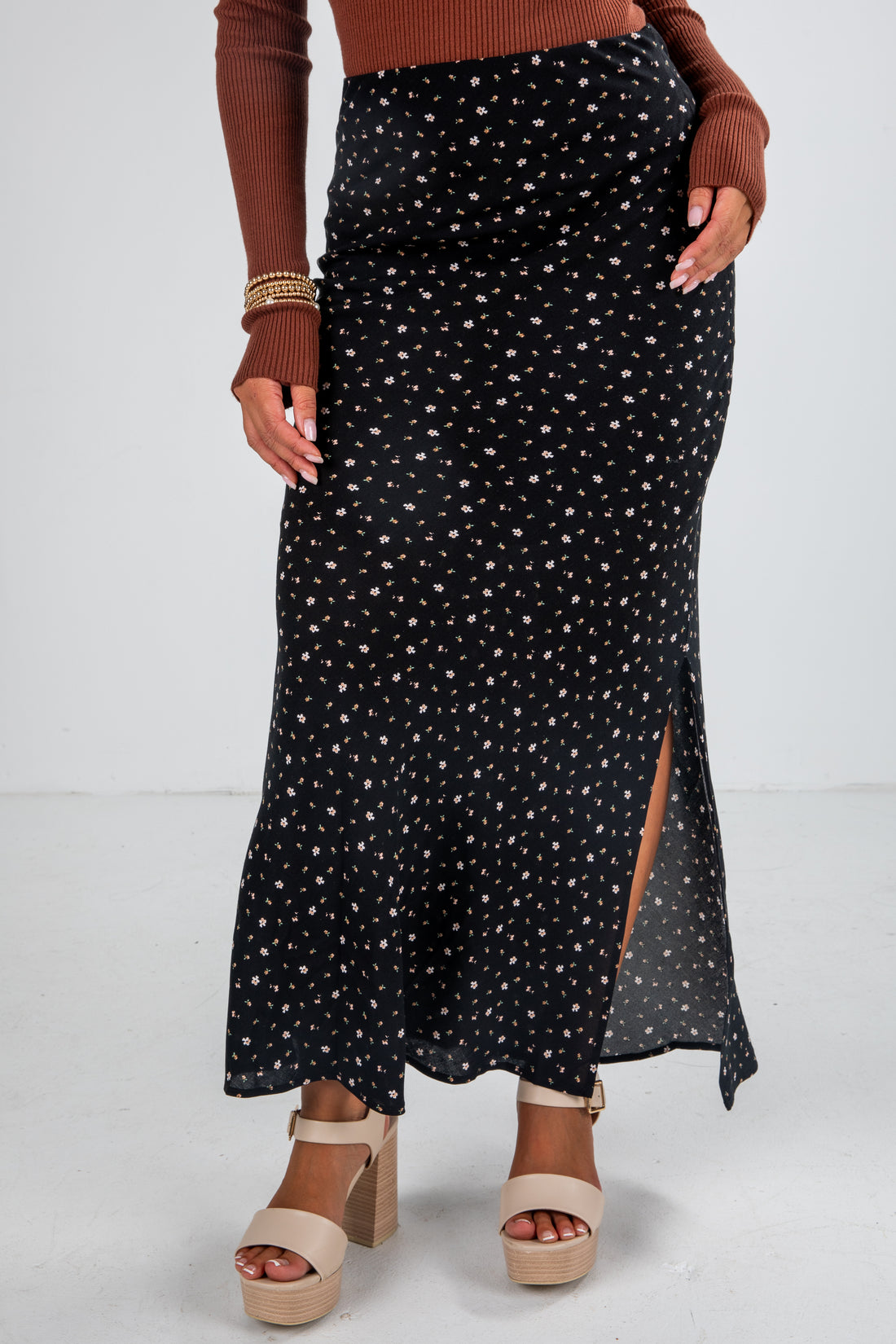 Person wearing a black patterned skirt with a brown top and sandals on a white background