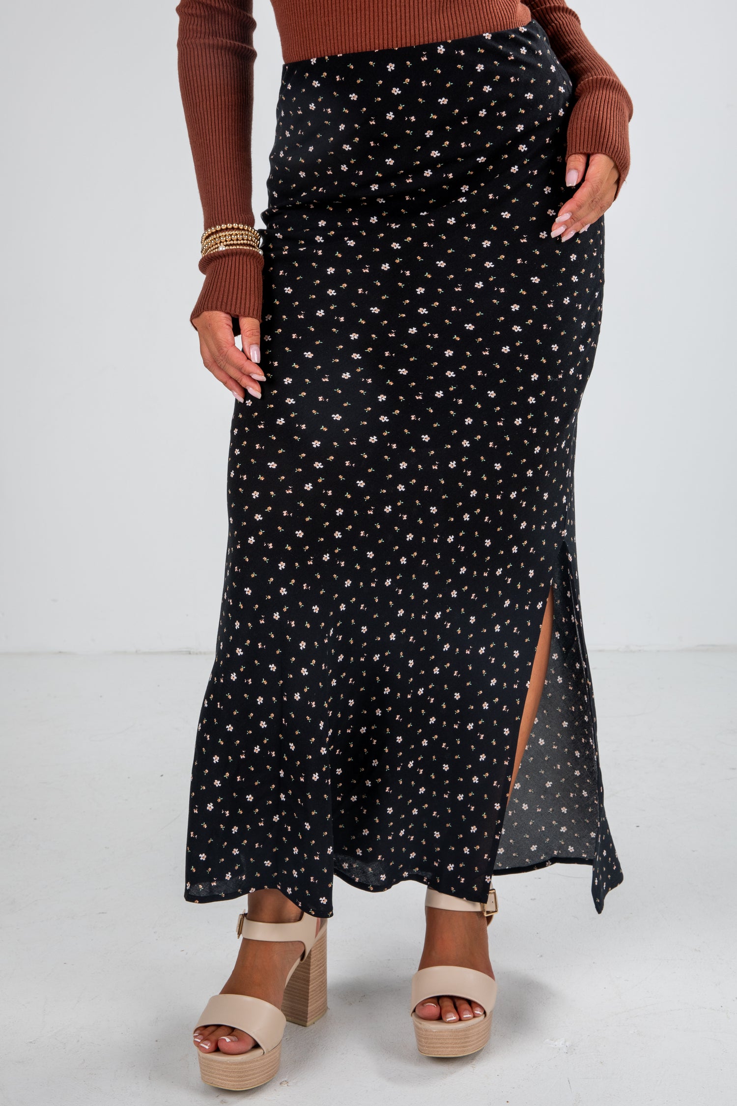Person wearing a black patterned skirt with a brown top and sandals on a white background