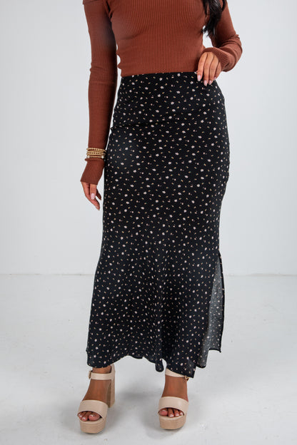 Person wearing a black polka dot skirt with a brown top on a white background