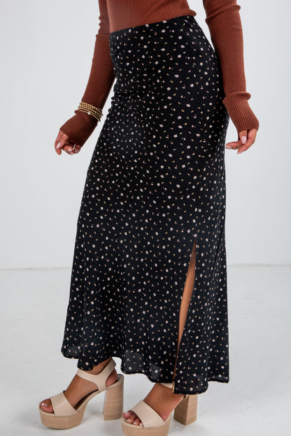 Person wearing a black patterned skirt with a brown sweater and beige sandals on a white background