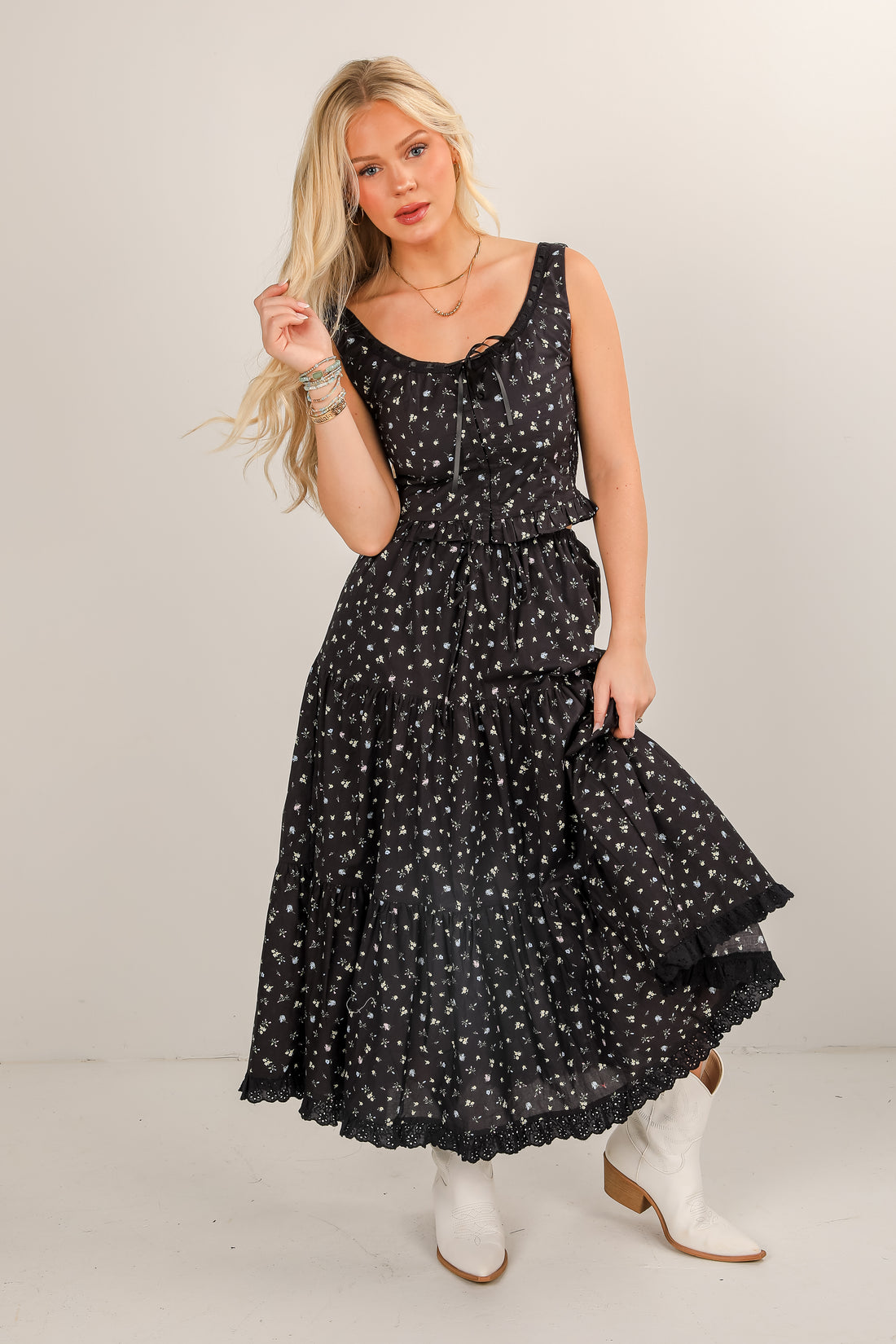 Woman wearing a black floral dress with white boots on a plain background