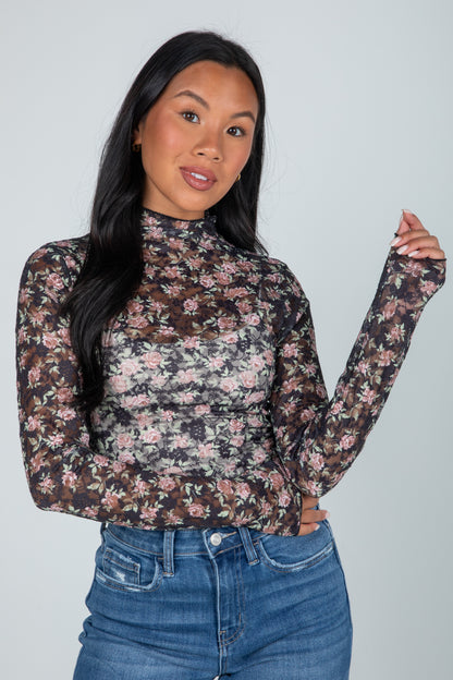 Woman wearing a floral long-sleeve top and jeans against a plain background