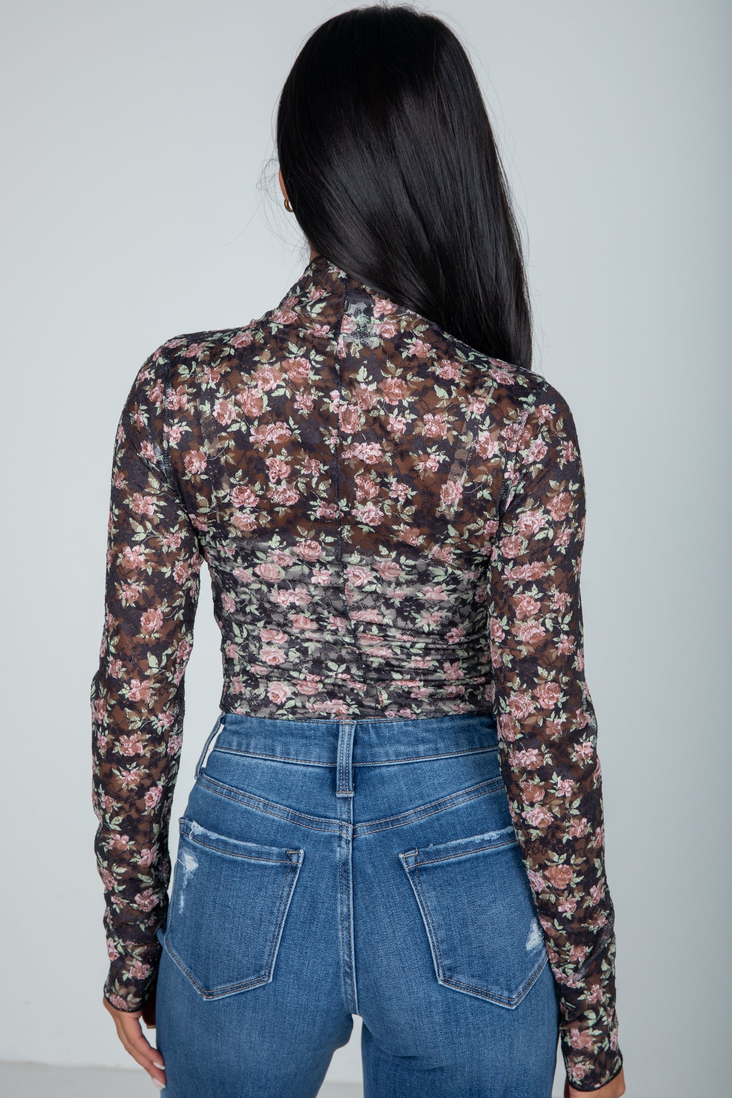 Person wearing a floral long-sleeve top and blue jeans against a plain background