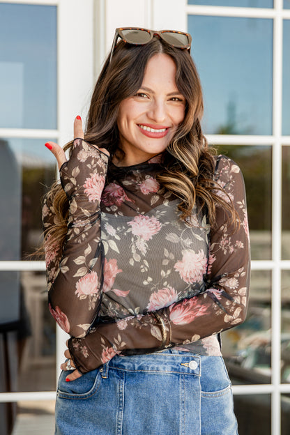 Woman wearing a floral long-sleeve top and jeans outdoors.