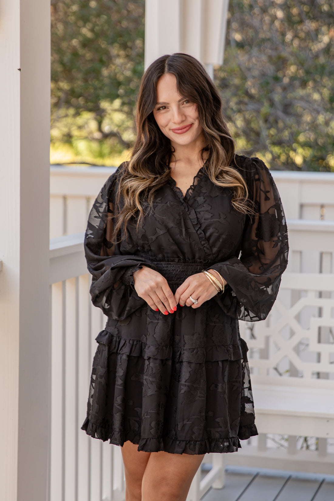 Woman wearing a black dress with sheer sleeves on a porch