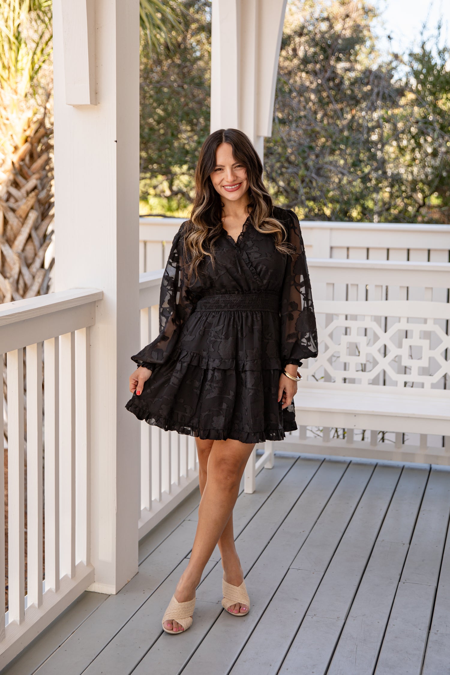 Woman in a black dress standing on a wooden porch with white railings.