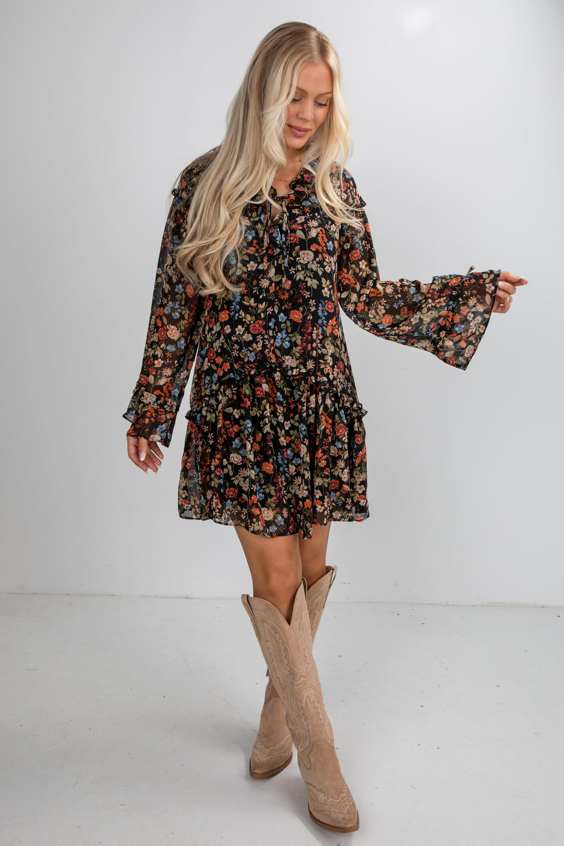 Woman wearing a floral dress with bell sleeves and beige knee-high boots on a white background