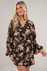 A woman modeling a black long-sleeve mini dress with a warm orange and beige floral pattern, featuring a wrap-style V-neckline and a matching fabric tie belt at the waist.