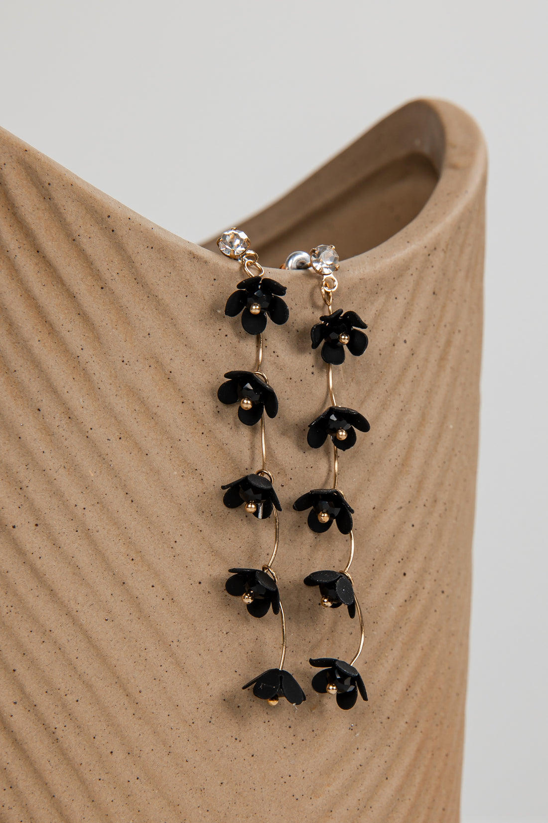 Black floral earrings on a beige stand with a neutral background