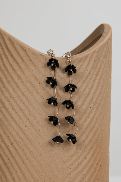 Black floral earrings on a beige stand with a neutral background