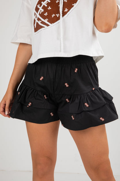 Black ruffled shorts with pink embellishments worn by a person on a white background