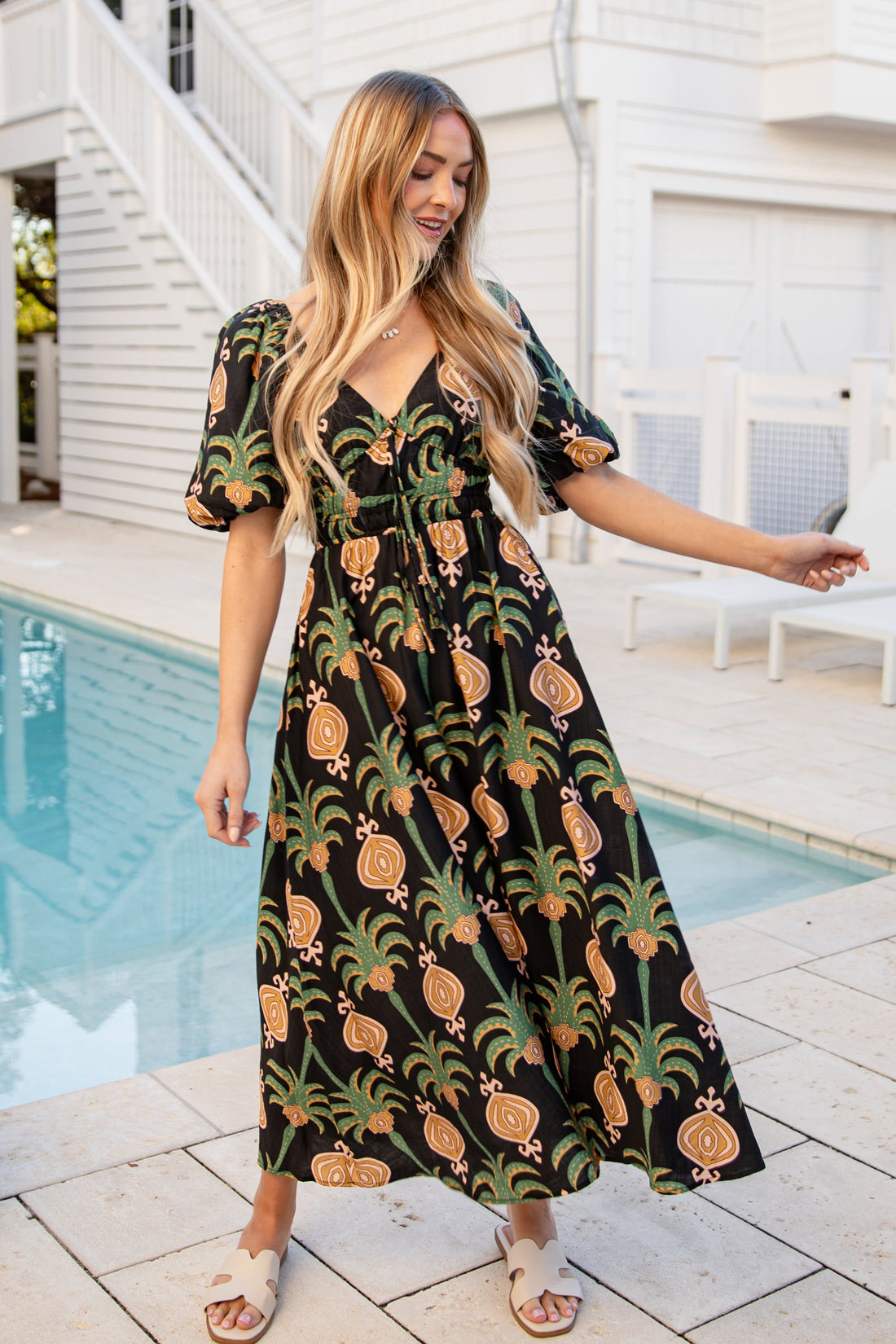 Woman in a pineapple-patterned dress standing by a poolside.