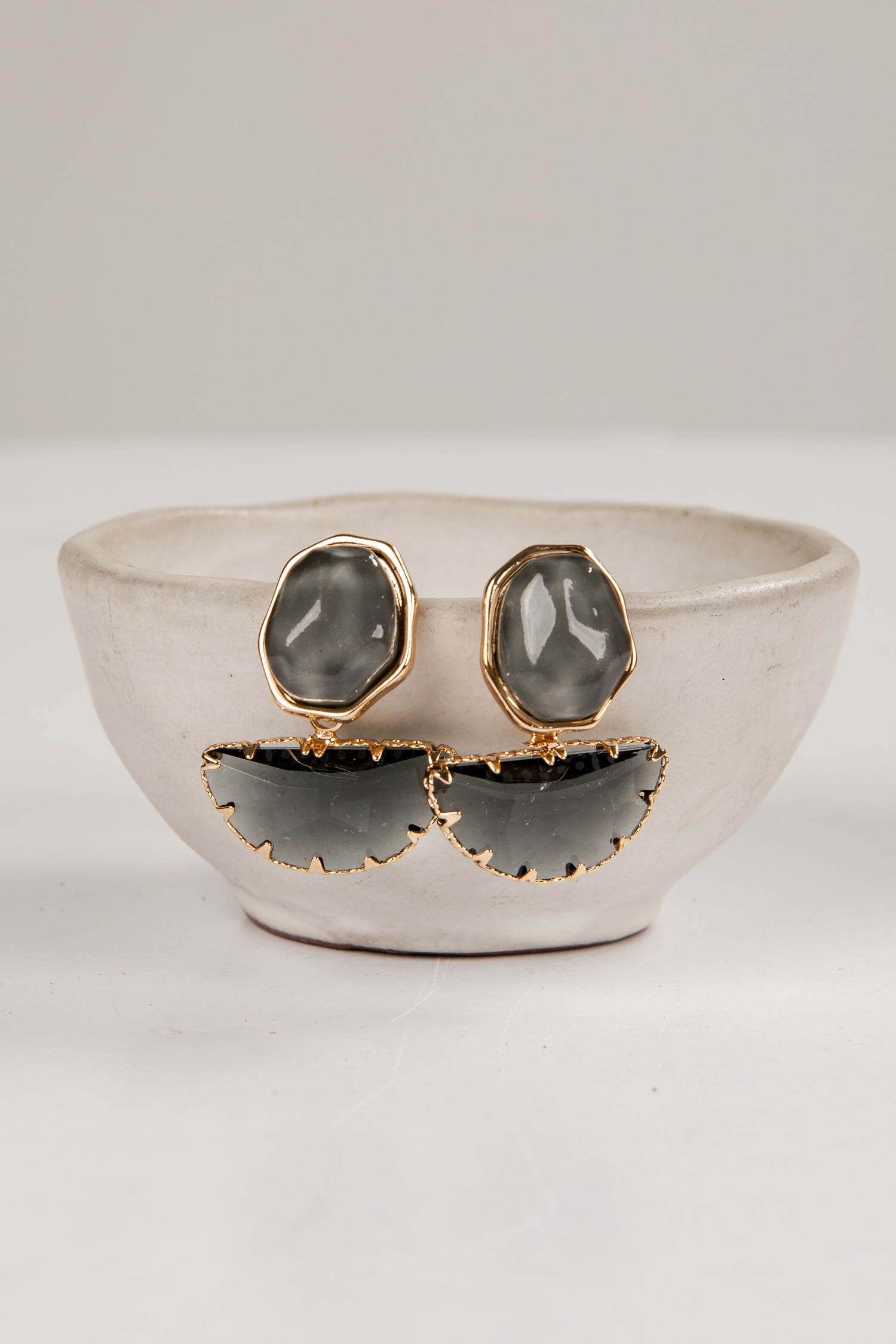 Pair of earrings with gray stones and gold accents on a white surface.