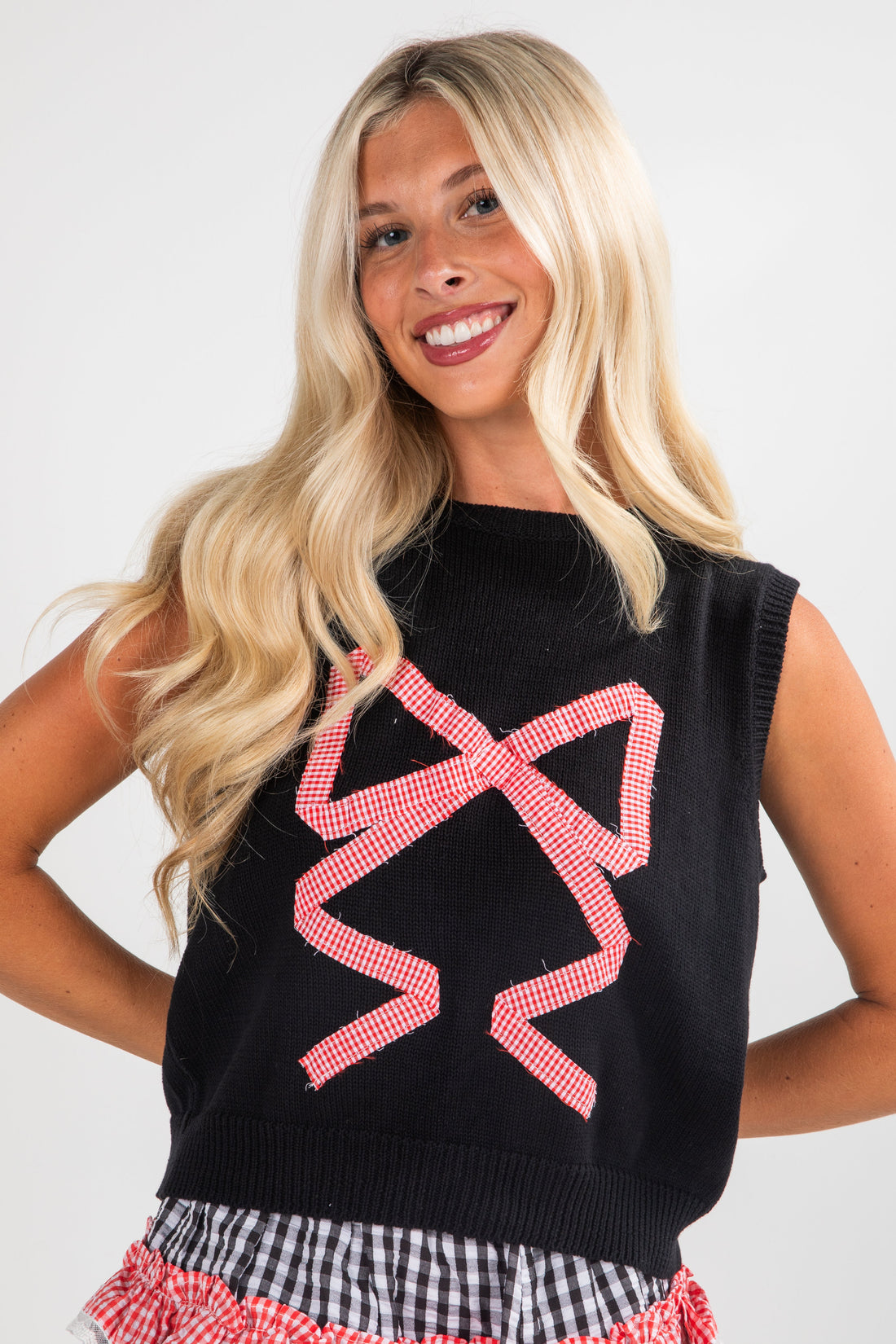 Woman wearing a black sleeveless sweater with pink geometric patterns on a white background