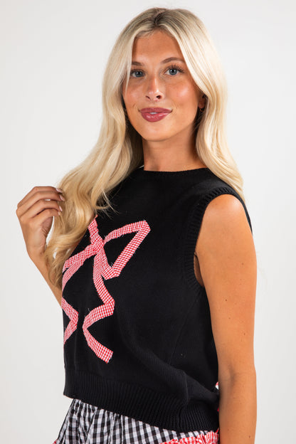 Woman wearing a black sleeveless top with pink designs against a white background