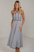A woman modeling a sleeveless halter-neck midi dress with a black and white gingham pattern and black trim, standing against a plain white studio wall.