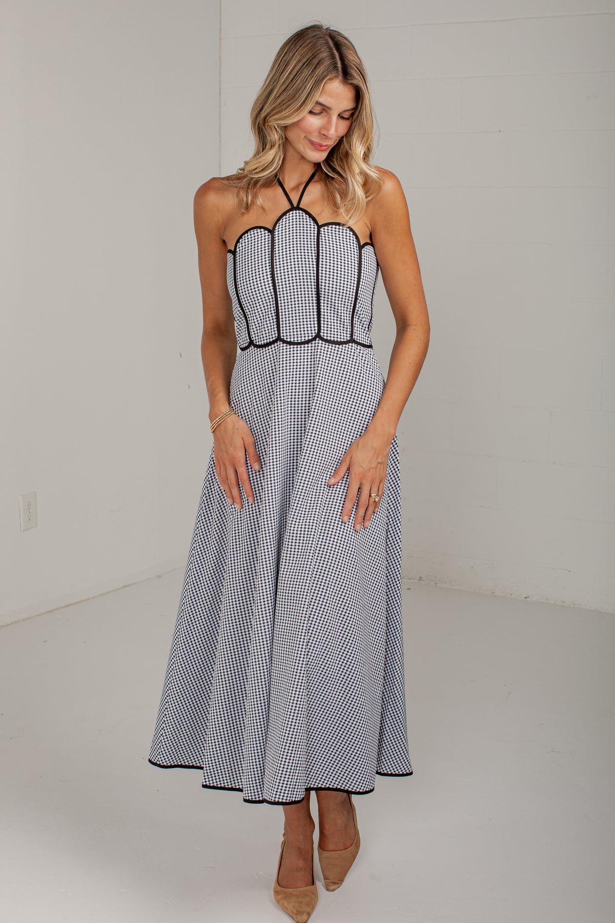 A woman modeling a sleeveless halter-neck maxi dress with a black and white gingham pattern, black trim, and a structured corset-style bodice, set against a plain white studio background.