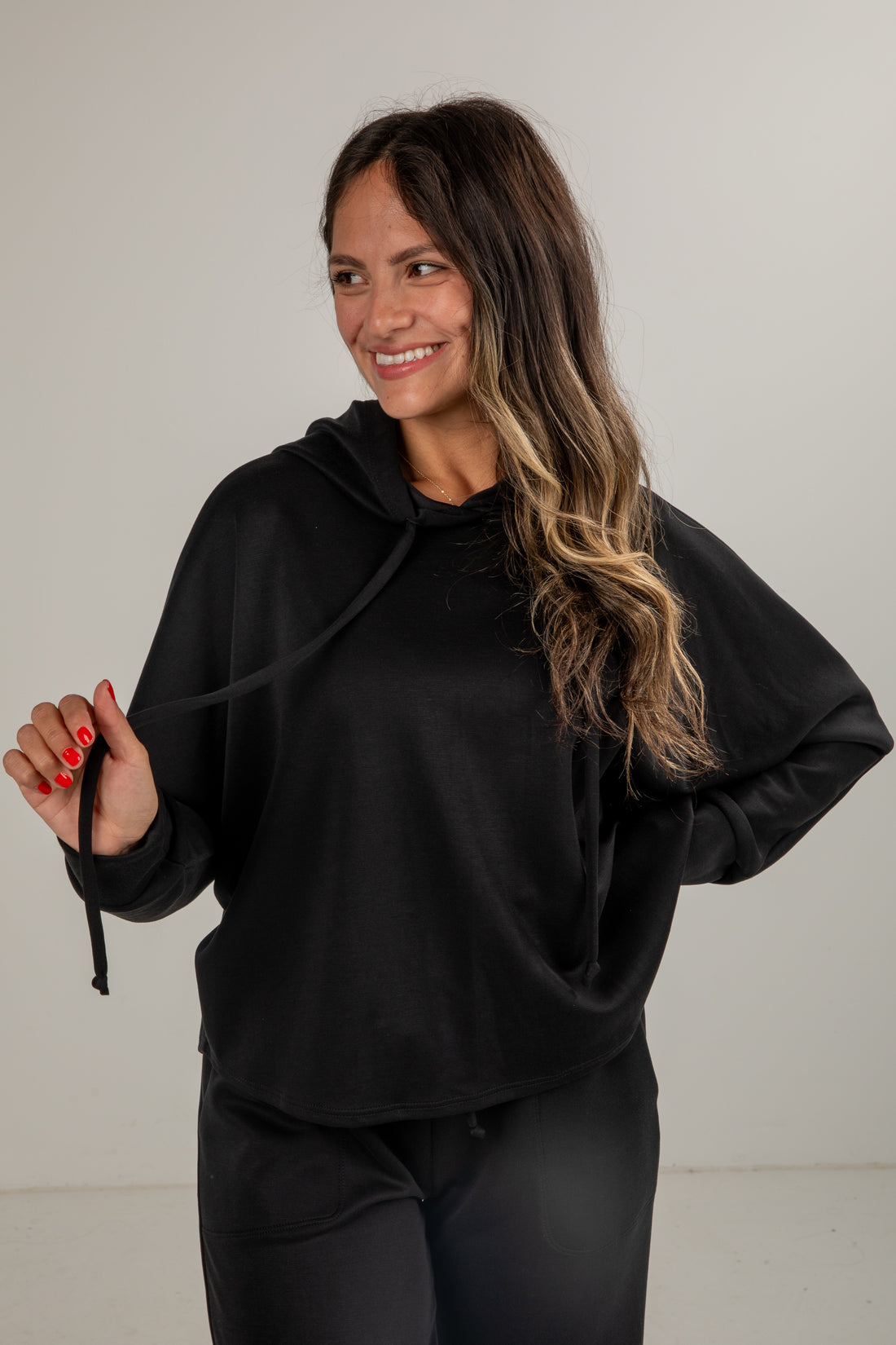 Woman wearing a black hoodie and pants against a plain background