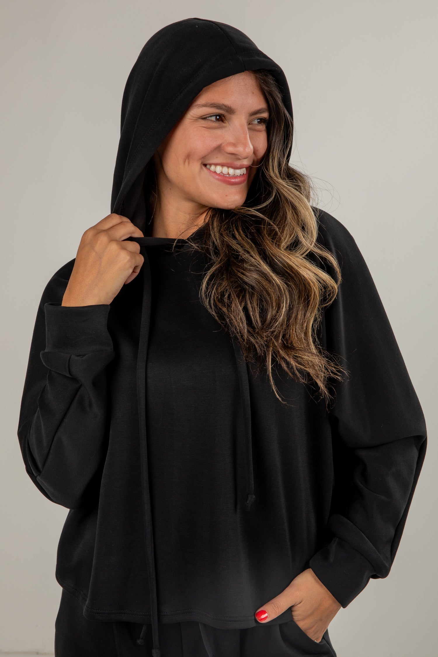 Woman wearing a black hooded outfit against a plain background