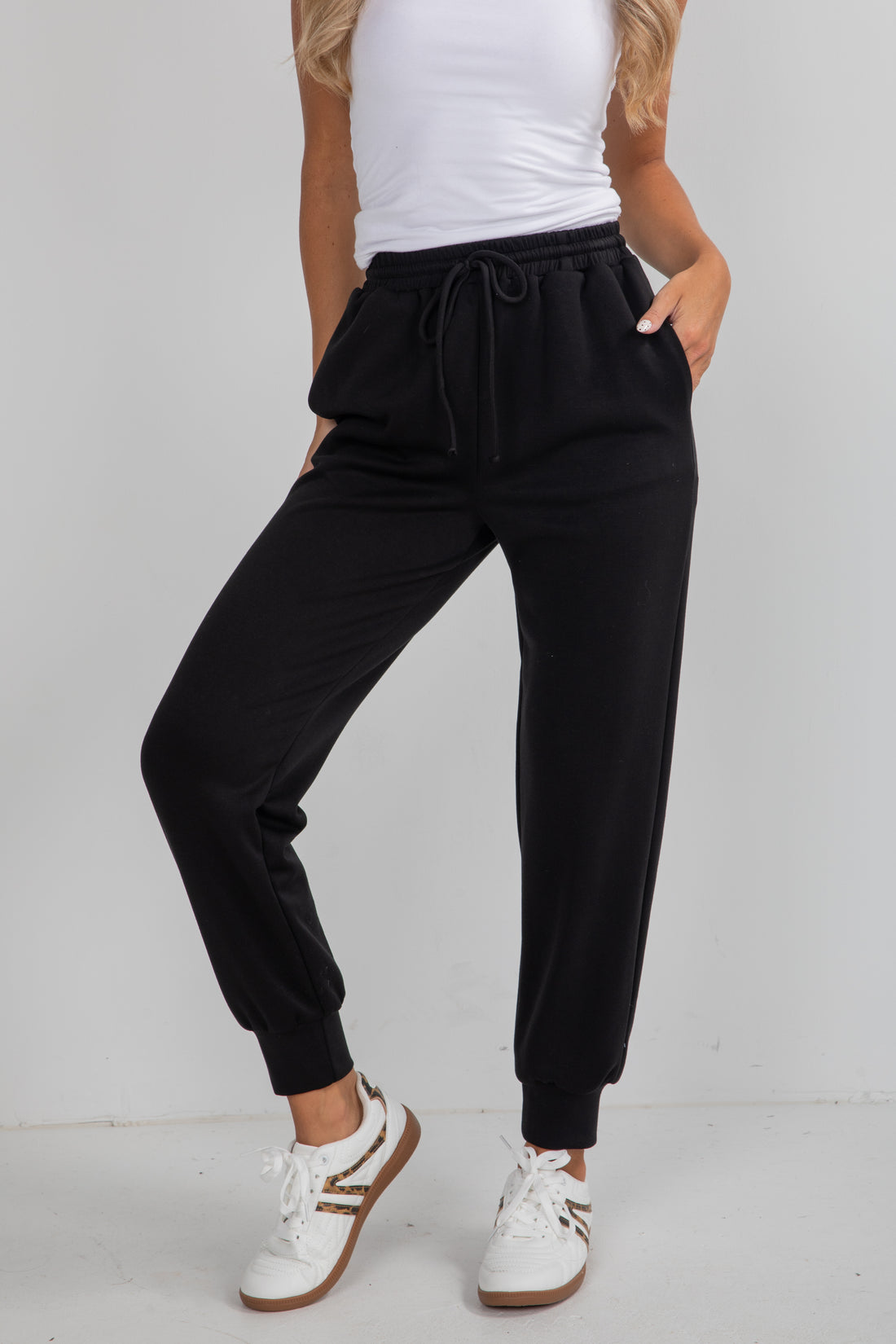 Person wearing black jogger pants and white sneakers on a plain background