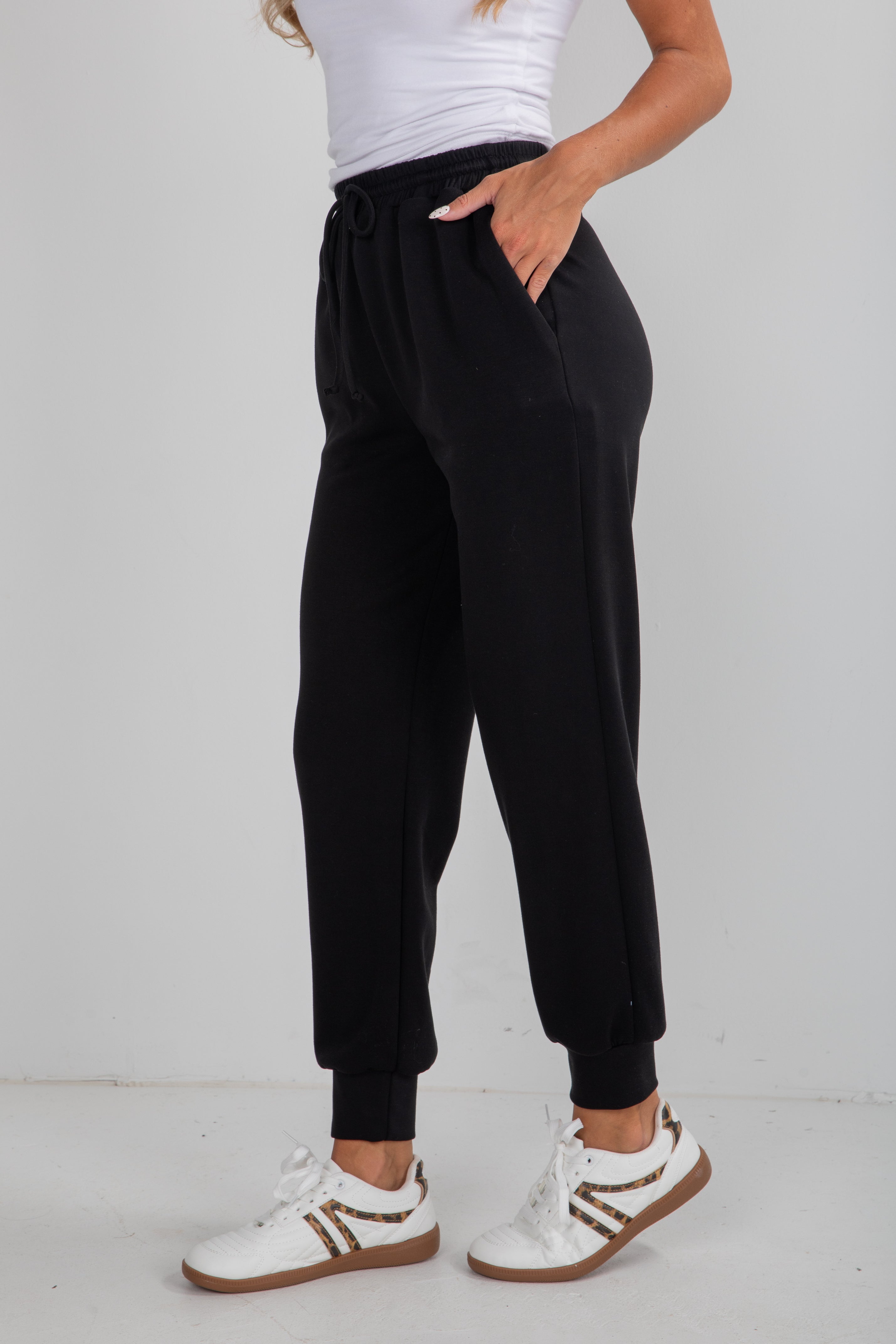 Person wearing black jogger pants and white sneakers on a plain background