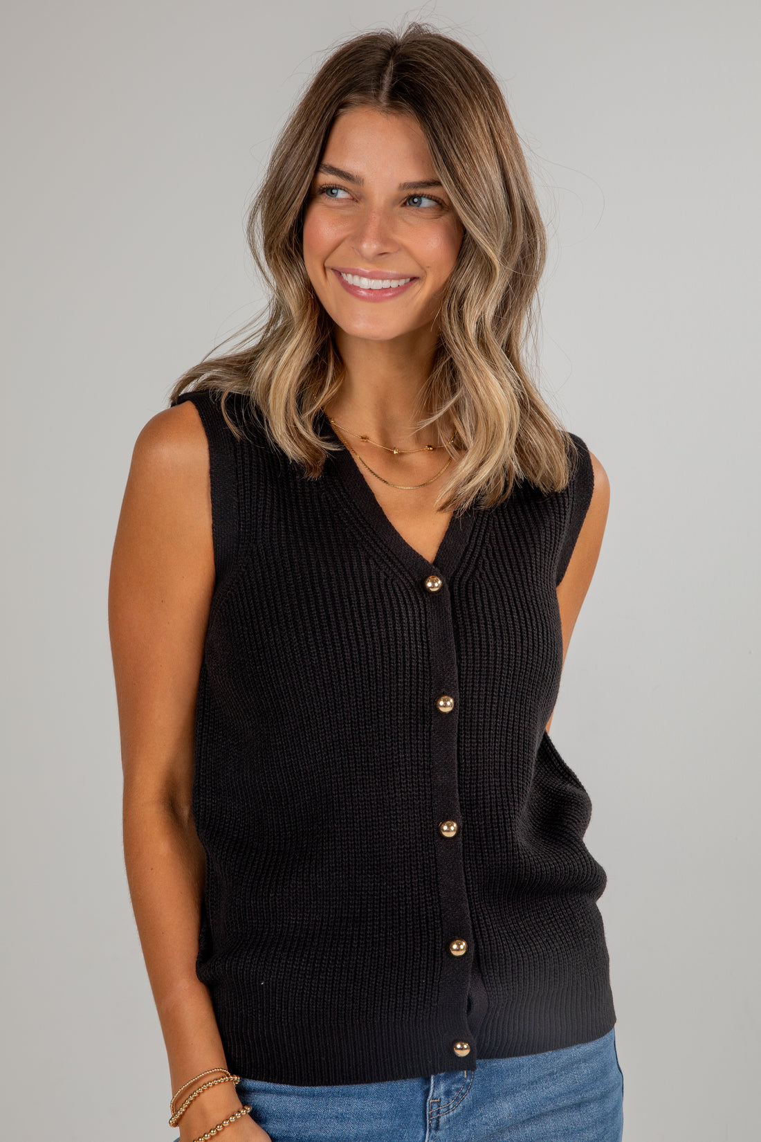 Woman wearing a black sleeveless button-up top against a gray background