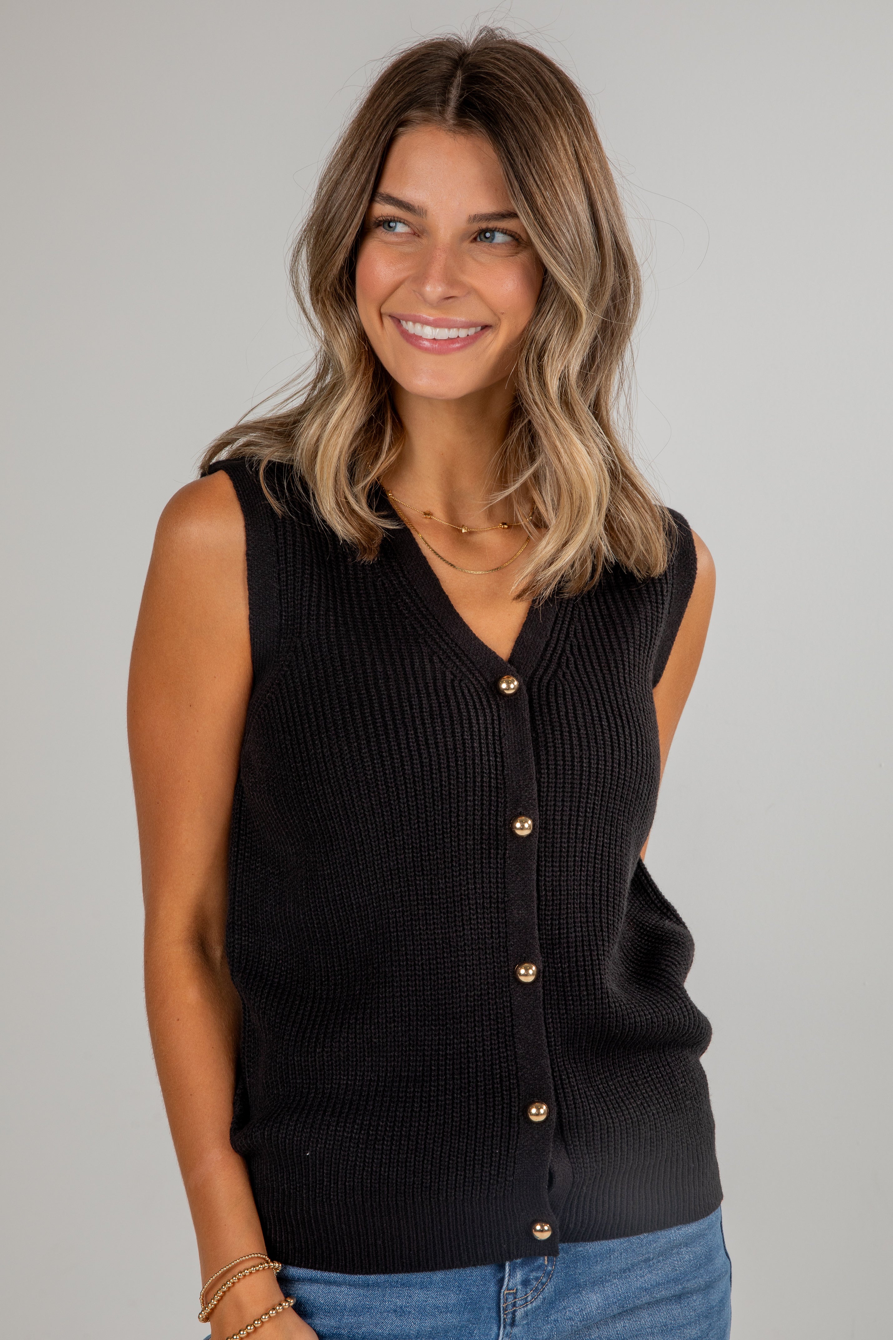 Woman wearing a black sleeveless button-up top against a gray background