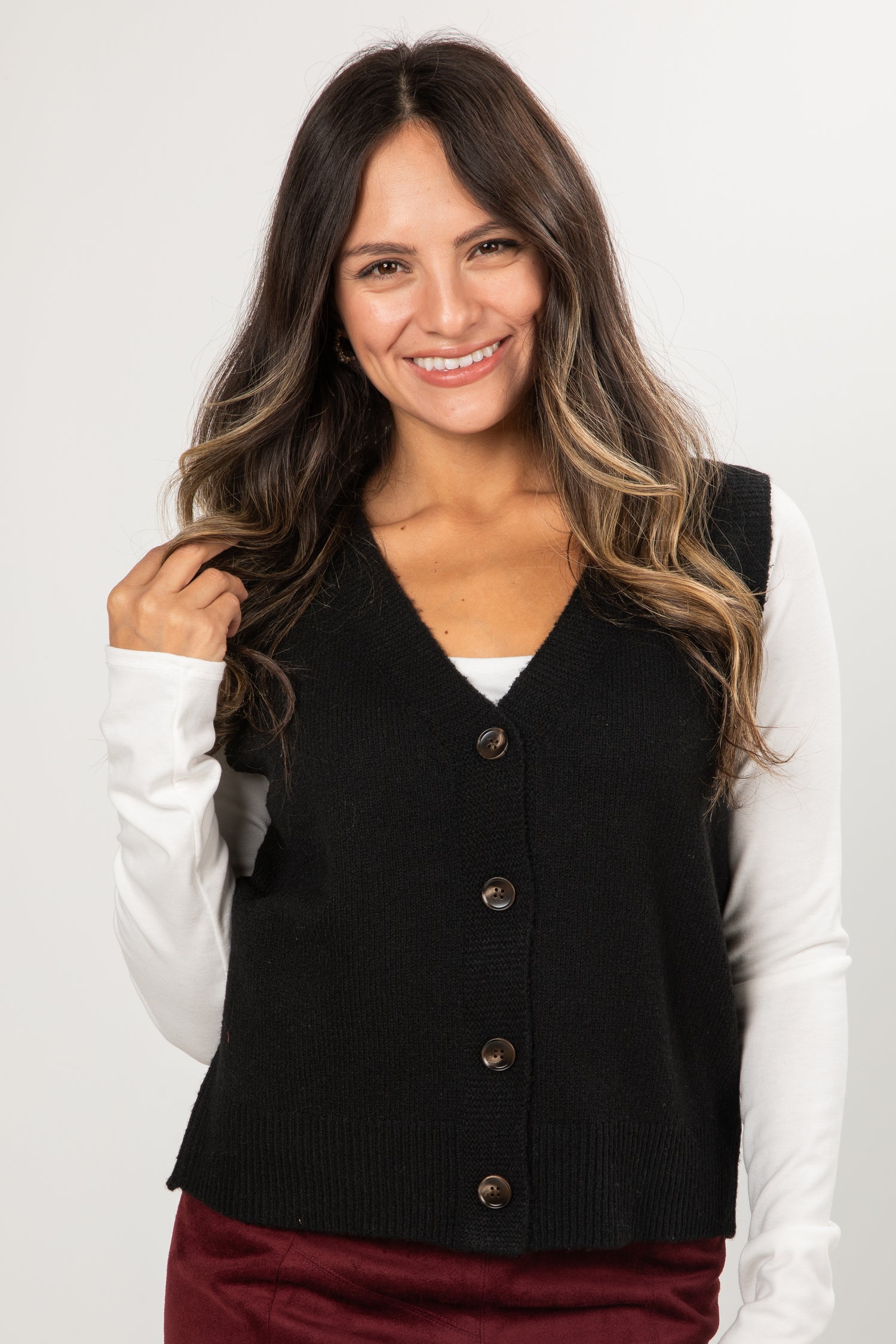 Woman wearing a black vest over a white long-sleeve shirt on a plain background